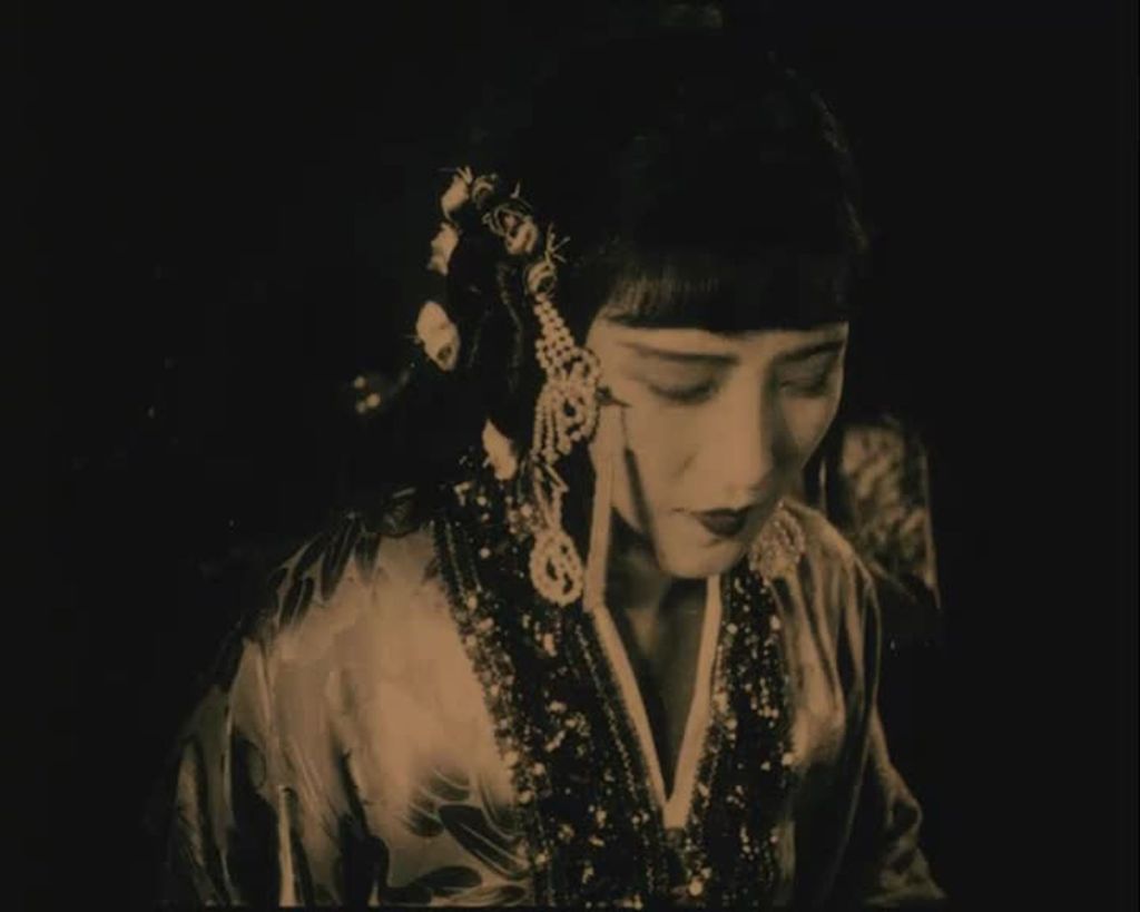 A woman is wearing traditional Chinese clothes. Her hair is dark, straight, down and there is a fringe. She is wearing make up and her lipstick stands out.