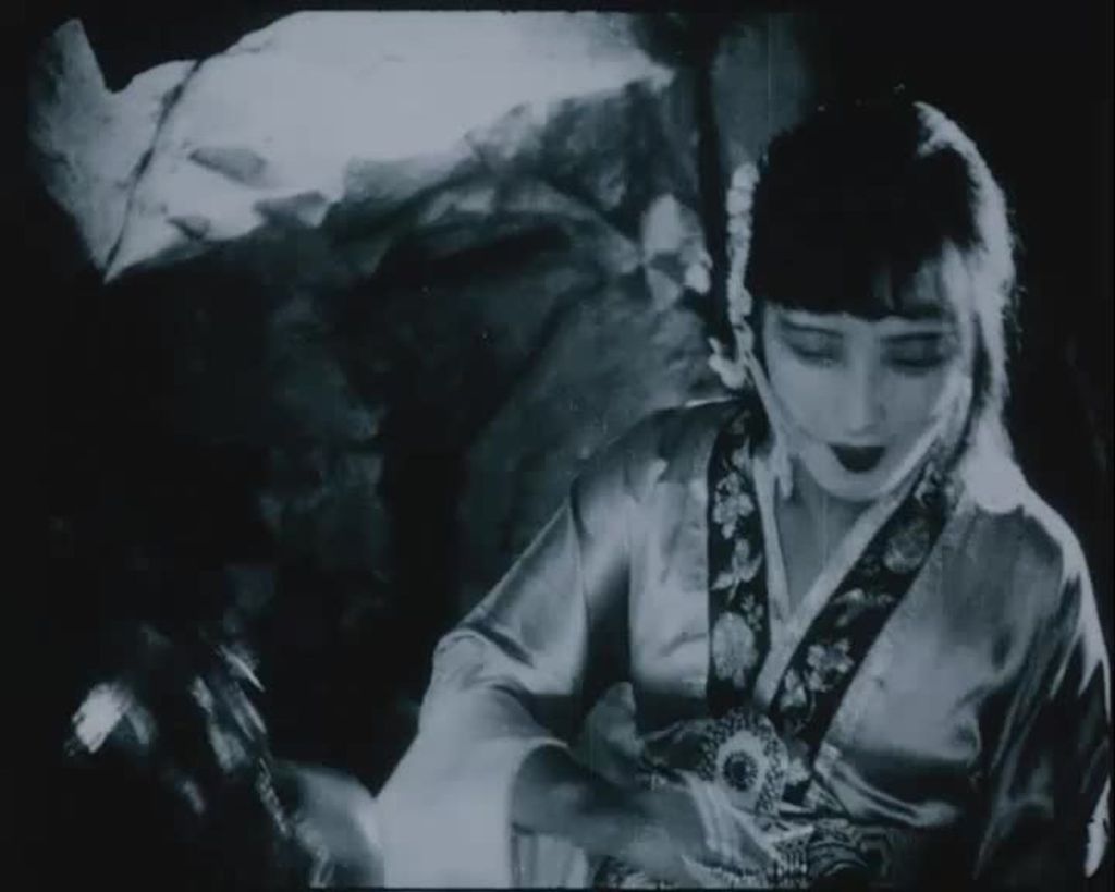 A woman is wearing traditional Chinese clothes. Her hair is dark, straight, tied and there is a fringe. 