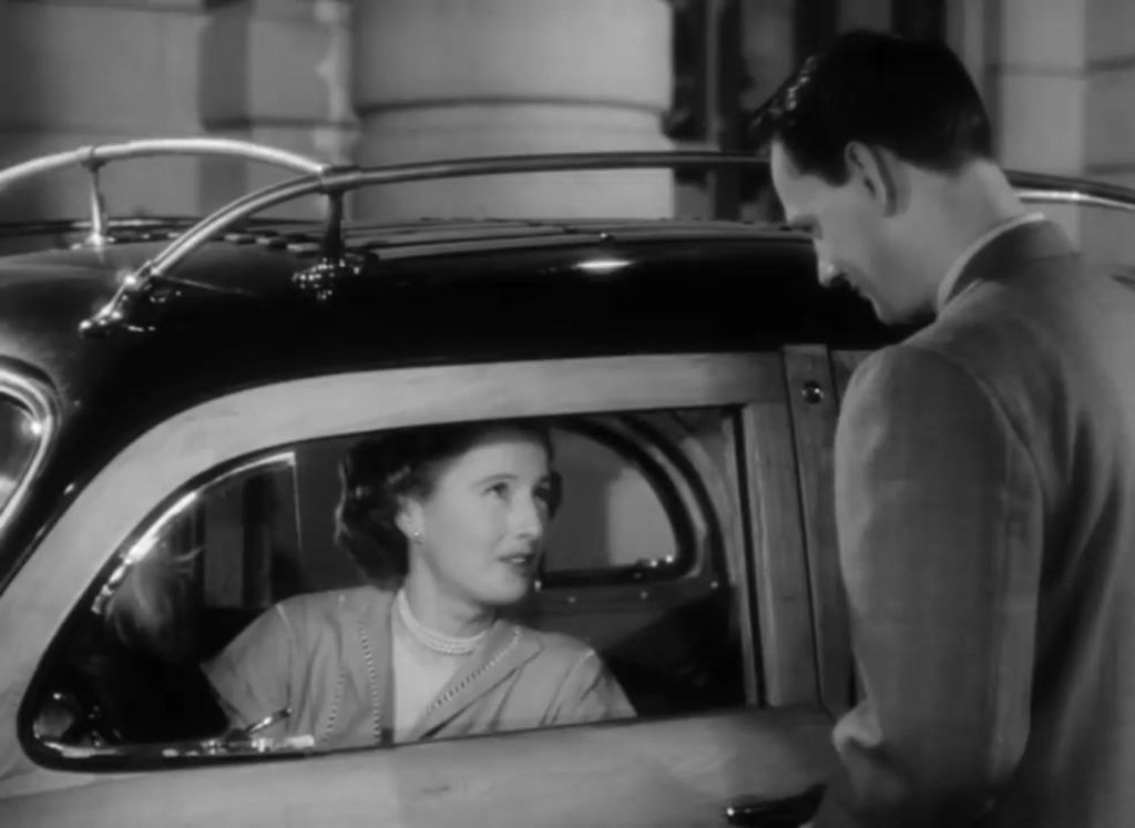 A woman is sitting in a car and talking to a man who is standing out of the car.
